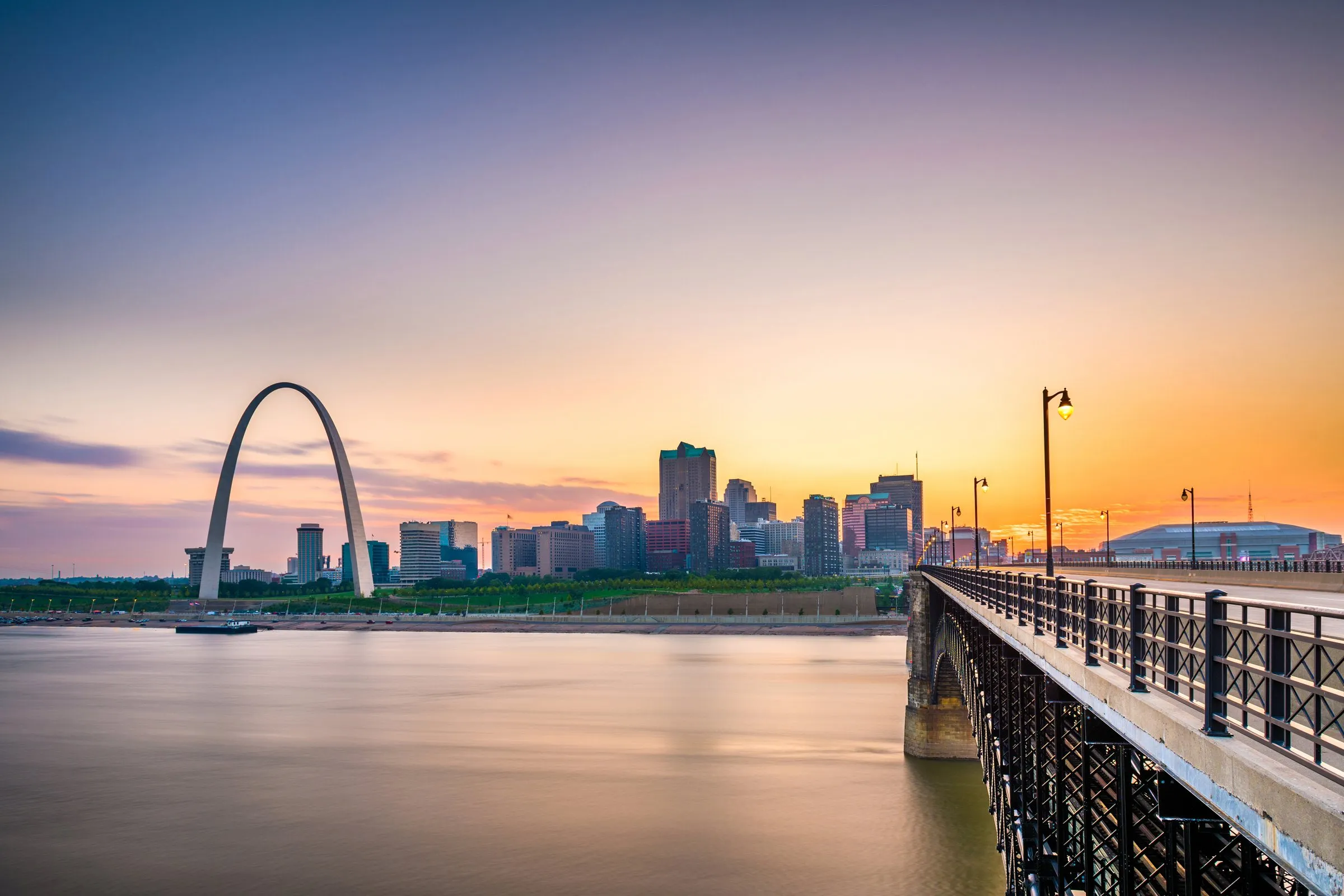 Downtown St. Louis skyline and the Gateway Arch at sunset, seen across the Mississippi River from the Eads Bridge